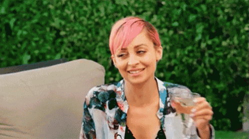 a woman with pink hair is holding a glass of wine while sitting on a couch .