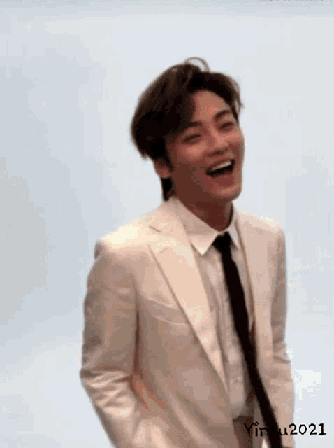 a man in a white suit and black tie is laughing and smiling .