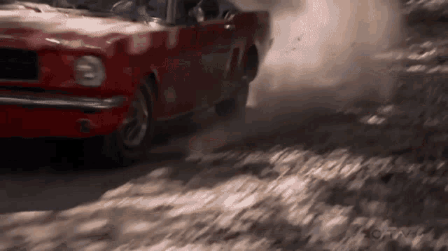 a red car is driving on a dirt road