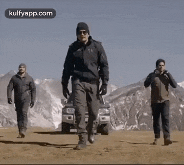a group of men are walking on a dirt road in front of a truck .