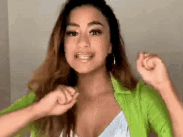 a woman wearing a green jacket and a white top is dancing and smiling .