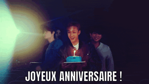 a man is holding a cake with a candle on it and the words joyeux anniversaire written below him