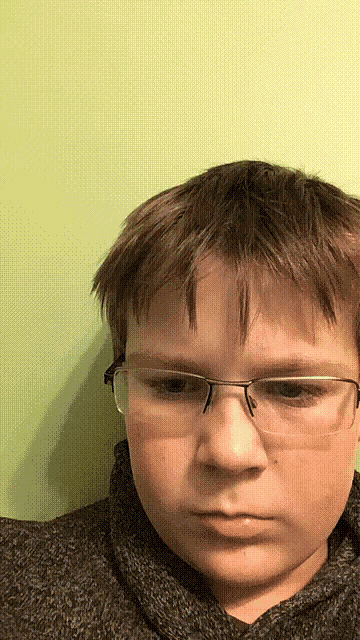 a young boy wearing glasses and a black sweater looks at the camera