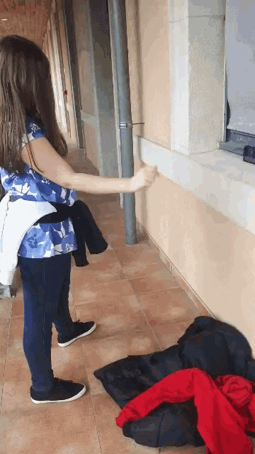 a girl in a blue shirt is standing in a hallway next to a window