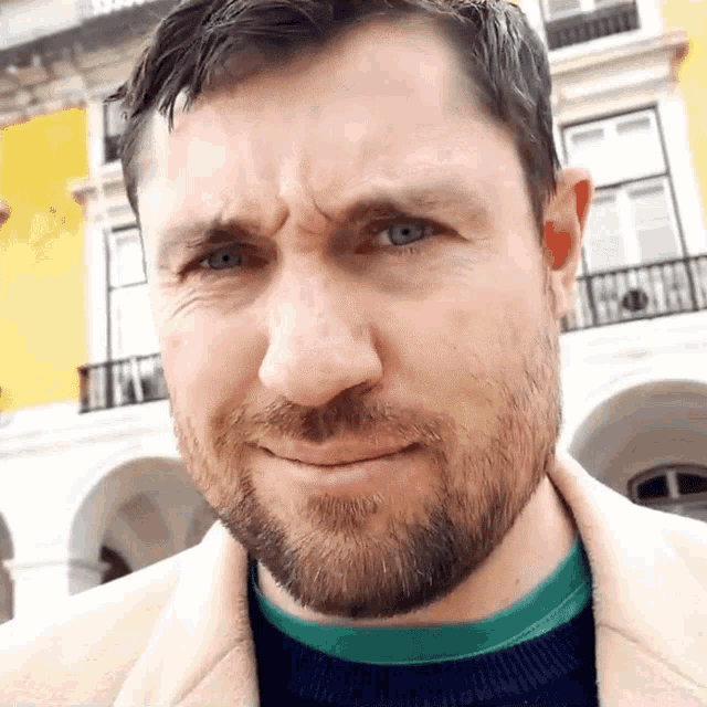a man with a beard is making a funny face in front of a yellow building