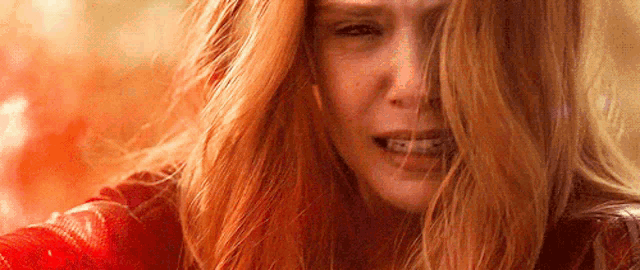 a close up of a woman 's face with red hair and a red background .