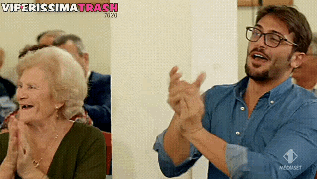 a man and a woman are clapping in front of a wall that says viperissima trash