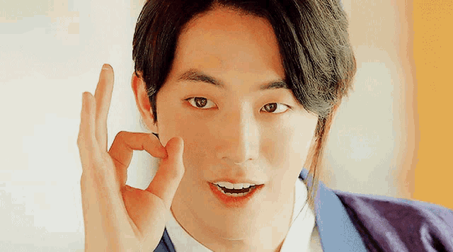a young man in a purple jacket is giving the ok sign