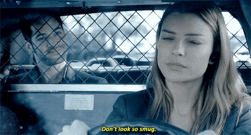 a man and a woman are sitting in a police car and the woman is saying " don 't look so smug " .