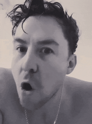 a black and white photo of a shirtless man making a surprised face