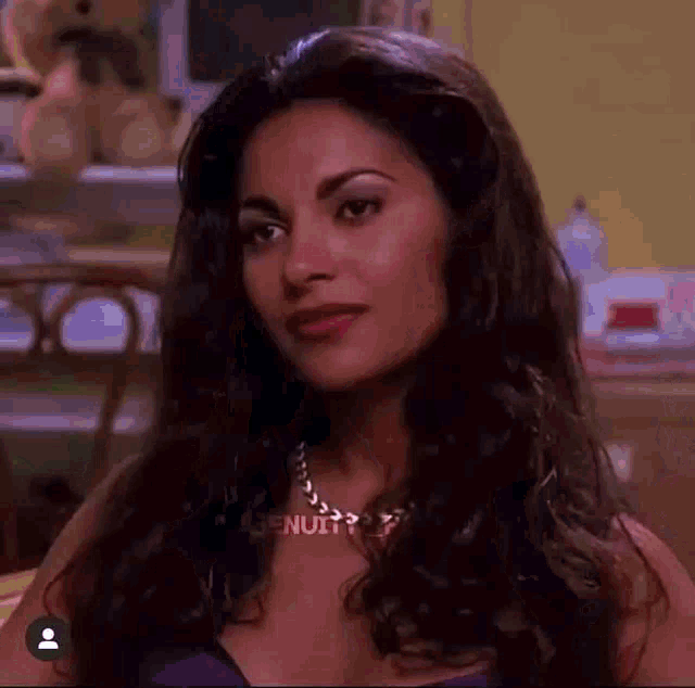 a woman with long dark hair and a necklace is sitting at a desk .