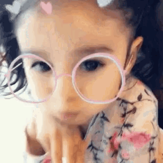 a little girl wearing glasses and a heart on her head is making a funny face .