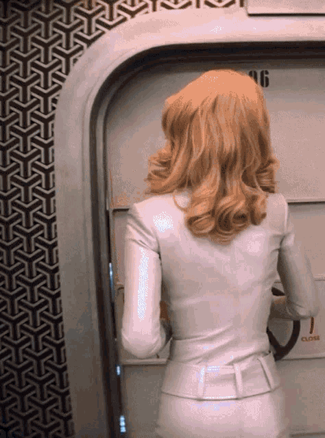 a woman in a white suit is standing in front of a door that has the number 96 on it