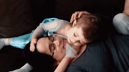 a little girl in a blue dress is laying on a woman 's stomach .