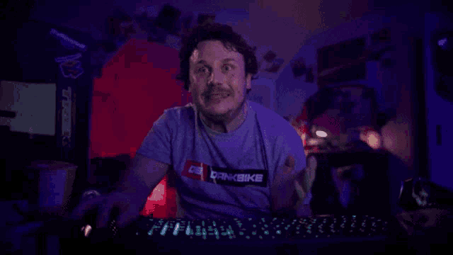 a man wearing a shirt that says bikebike is sitting at a computer keyboard
