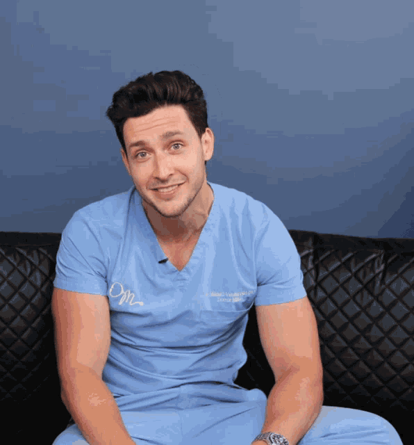 a man wearing a scrub top that says dm on it sits on a couch