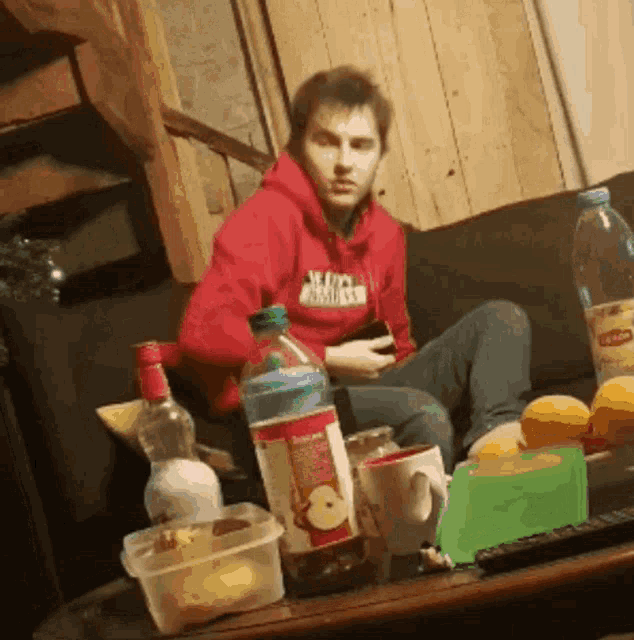 a man in a red hoodie is sitting on a couch with a bottle of apple juice in front of him