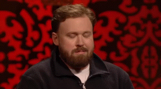 a man with a beard is sitting in front of a red background and looking at the camera .