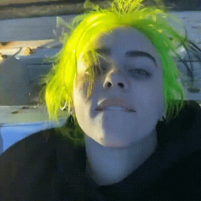 billie eilish with neon green hair is making a funny face .