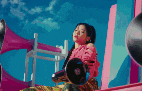 a woman in a pink shirt is holding a megaphone in front of a blue sky
