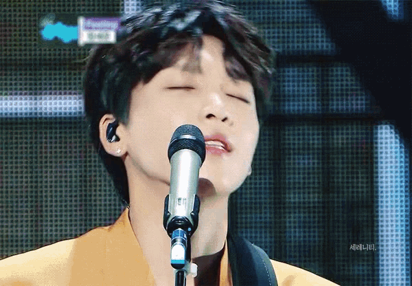 a close up of a person singing into a microphone with their eyes closed in front of a screen