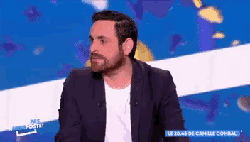 a man with a beard is sitting on a stage in front of a blue and white background .