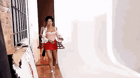 a woman in a pink top and red shorts is walking down a hallway holding a purse .