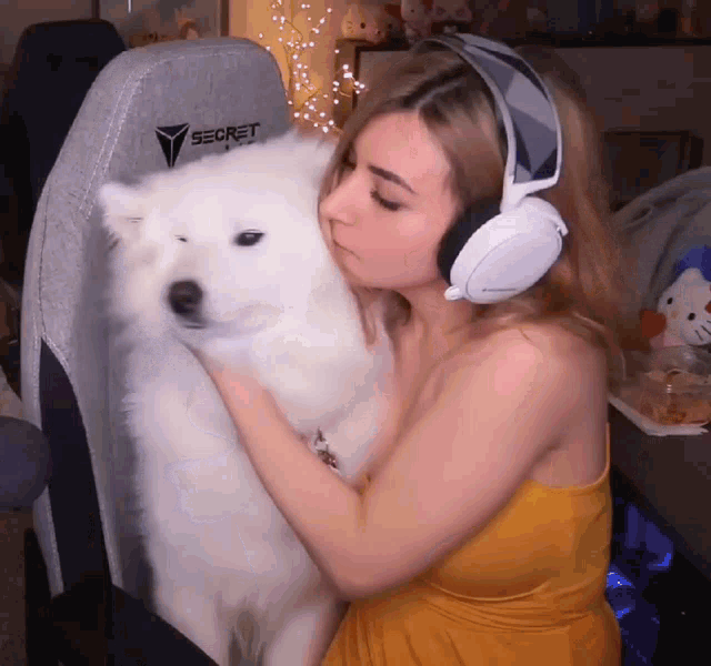a woman wearing headphones is holding a white dog in front of a secret gaming chair