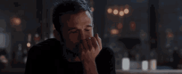 a man covering his mouth with his hand while sitting at a bar