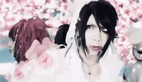 a woman in a bride costume is standing in front of a wall of pink flowers .