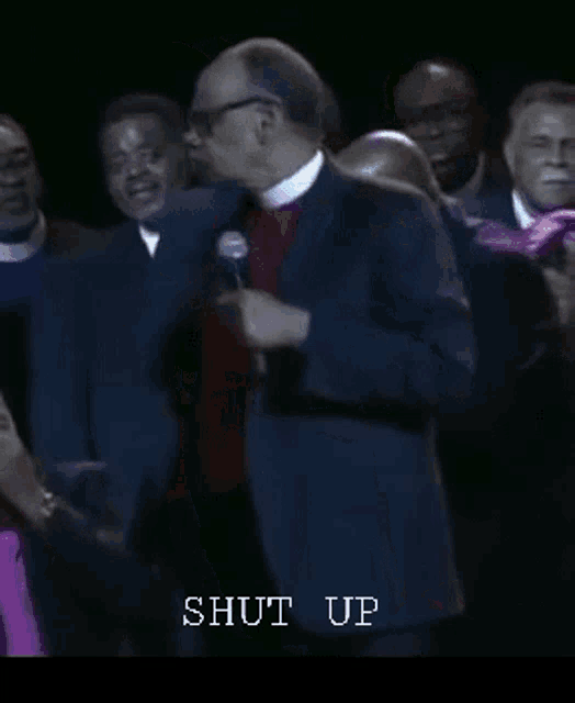a group of people are standing around a man holding a microphone with the words shut up written below him