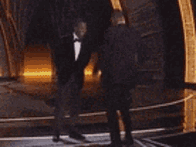 two men in tuxedos are dancing on a stage at an event .
