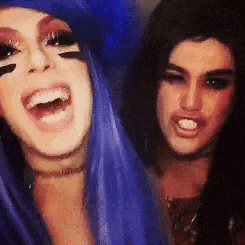 two drag queens are posing for a picture together and one of them is wearing blue hair .