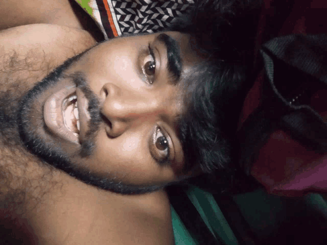a man with a beard is laying on a bed and making a funny face