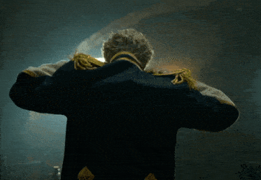 a man in a military uniform stands in a dark room with his arms outstretched