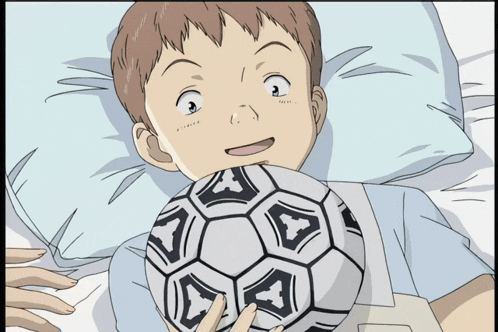 a young boy is laying on a bed holding a soccer ball