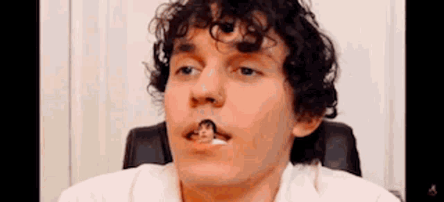 a man with curly hair is sitting in a chair with his mouth open and a small person sticking out of his mouth .