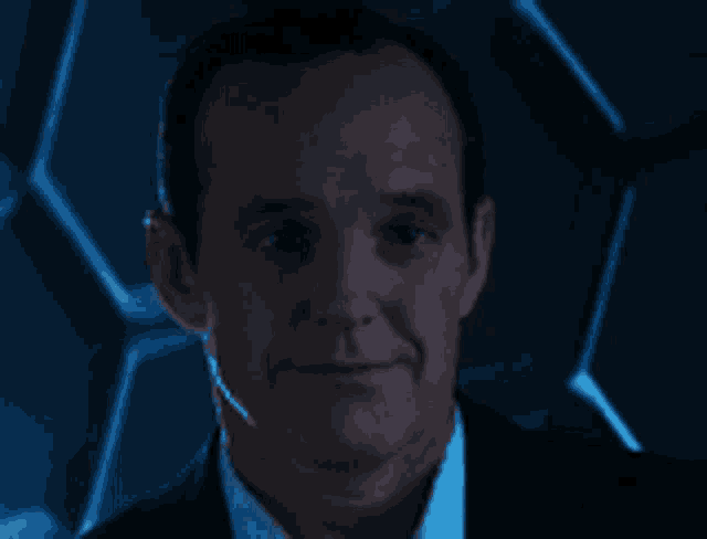 a man in a suit and tie is smiling in front of a blue wall
