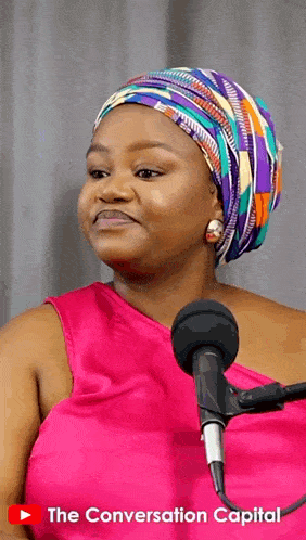 a woman wearing a head scarf stands in front of a microphone with the conversation capital written on the bottom right