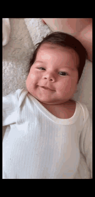 a baby is wearing a white bodysuit and smiling for the camera