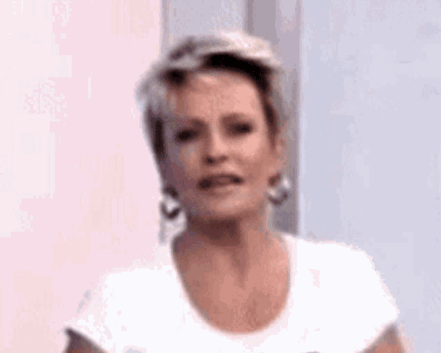 a woman wearing a white shirt and hoop earrings is making a funny face .