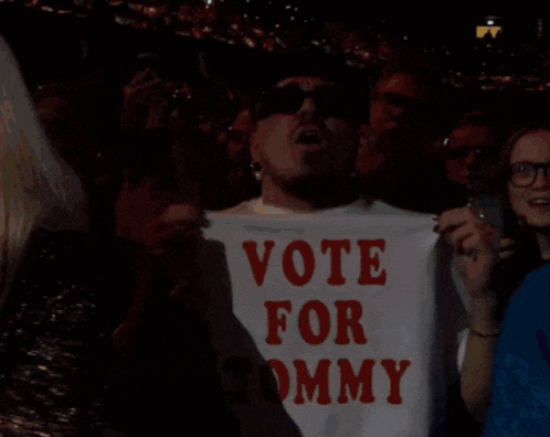 a man in a crowd holds up a sign that says vote for tommy