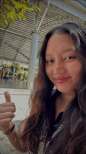 a woman giving a thumbs up and wearing a college shirt