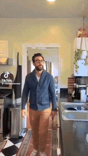 a man in a blue jacket and brown pants is walking in a kitchen with a tiktok logo on the bottom