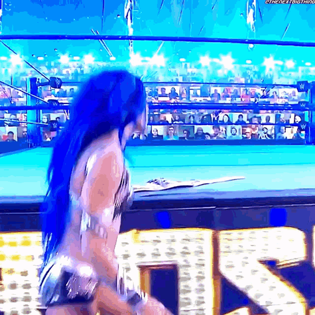 a woman with blue hair is standing in a wrestling ring in front of a crowd