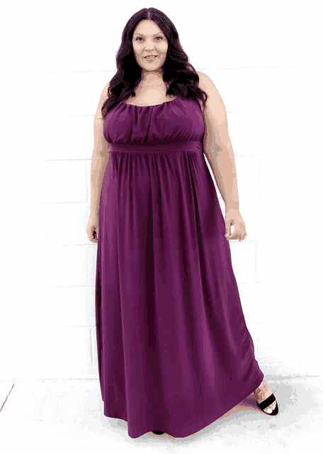 a woman in a purple dress is standing in front of a white brick wall
