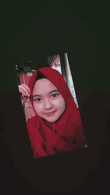a woman wearing a red hijab is taking a picture of herself