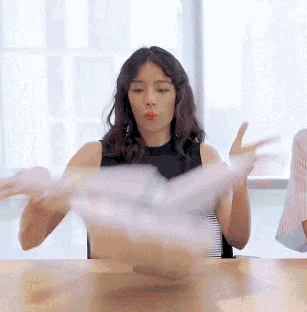 a woman sitting at a table blowing a kiss while holding a bag of food