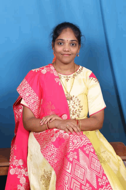 a woman wearing a pink and yellow dress is sitting on a bench