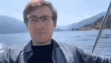 a man wearing glasses is riding on the back of a boat in the water .